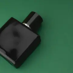 Czarna butelka perfum z nutami **vetiver** na zielonym tle.
