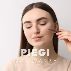 Kobieta z piegami na twarzy delikatnie poprawia makijaż.