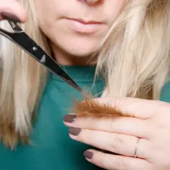 Kobieta z blond włosami pokazuje, jak obciąć włosy, trzymając nożyczki przy końcówkach.