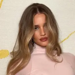 Kobieta z włosami w odcieniu honey blonde, w różowym golfie, na tle z żółtymi wzorami.