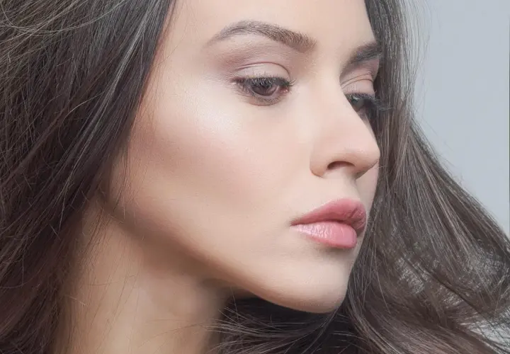 Delikatny profil kobiety z subtelnym makijażem. Zimne kolory podkreślają jej urodę, a włosy tworzą miękką ramę.