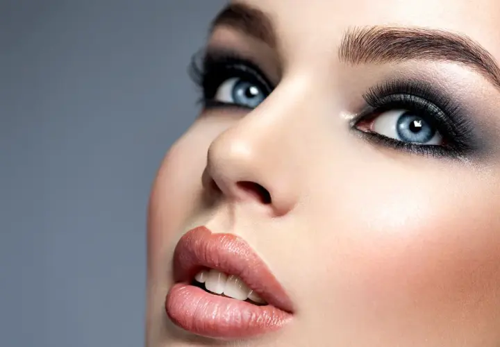 Intensywne smokey eyes podkreślają błękitne oczy modelki. Usta w odcieniu nude i perfekcyjna cera dopełniają makijaż.
