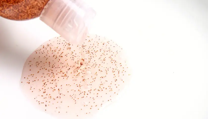 Przezroczysty żel z drobinkami, przypominający **mikroplastik w kosmetykach**, wypływa z butelki.