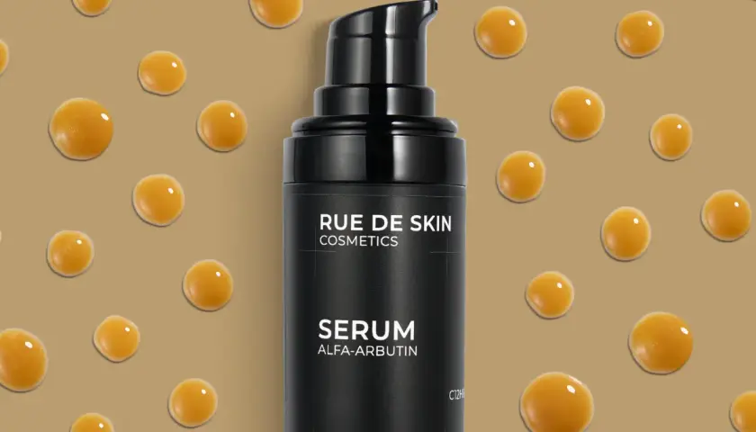Czarny flakonik serum z alfa-arbutyną, otoczony kropelkami o bursztynowym odcieniu.