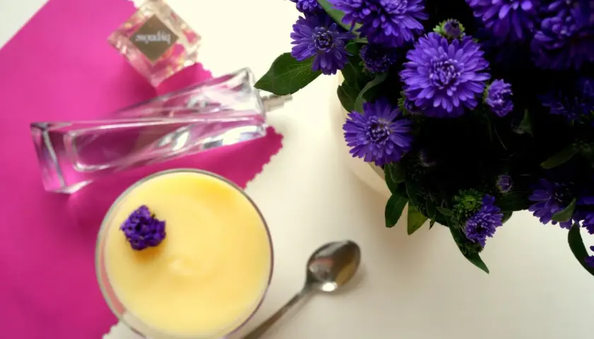 Perfumy "Hypnose" obok deseru i fioletowych kwiatów.