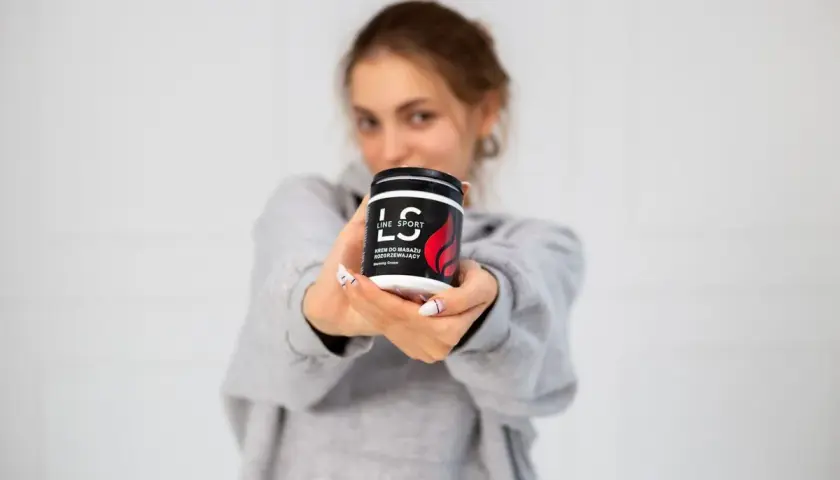 Młoda kobieta prezentuje krem do masażu rozgrzewający Line Sport. Idealny po treningu.