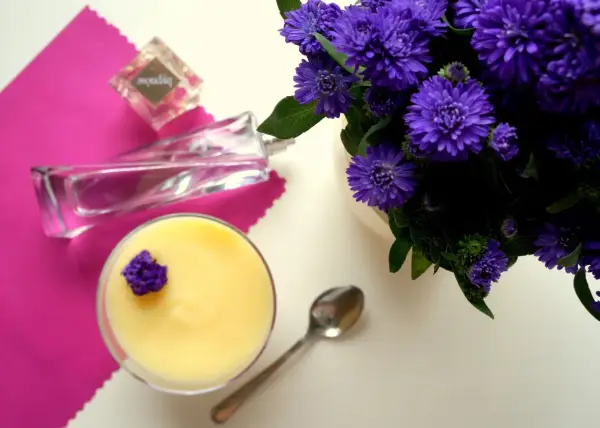 Perfumy "Hypnose" obok deseru i fioletowych kwiatów.